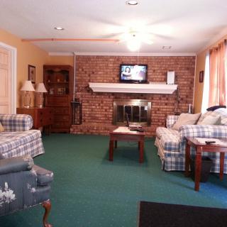 A cozy living room with a brick fireplace, plaid sofas, and a green carpet.