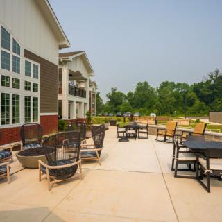An outdoor patio area with seating arrangements near a building, surrounded by greenery.