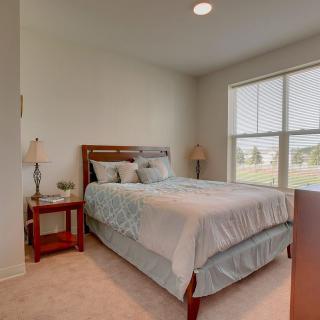 A cozy bedroom with a neatly made bed, bedside tables, and large windows allowing natural light in.
