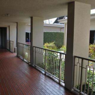 A covered outdoor corridor with railings overlooking a garden area.