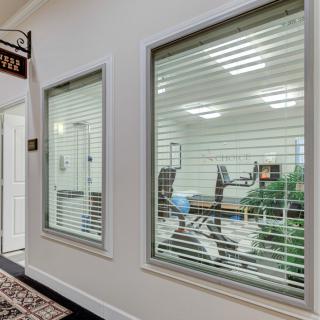 A view of an office interior with large windows and blinds, showcasing desks and chairs inside.
