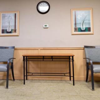 A tidy waiting room with two chairs, a table, a clock, and framed artworks on the wall.