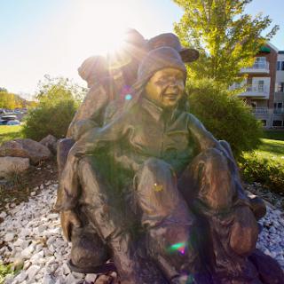 A bronze sculpture depicting joyful children playing together, illuminated by the warm sunlight.