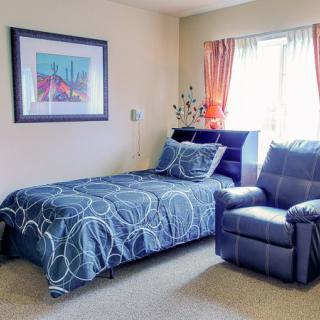 A cozy bedroom with a single bed, an armchair, and a decorative artwork on the wall.