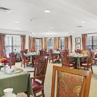A cozy dining room with multiple tables and chairs, decorated with warm colors and large windows with curtains.