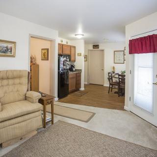 A cozy apartment interior featuring a living room with an armchair, connected to a small kitchen and dining area.