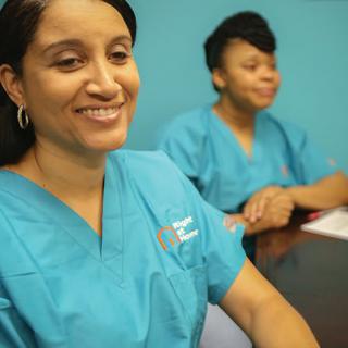 Two healthcare professionals in scrubs sit at a table, engaged in conversation.
