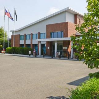 A building with flags, surrounded by trees and a parking lot on a sunny day.