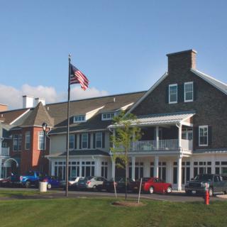 A large building with an American flag in front, surrounded by green grass and a clear sky.