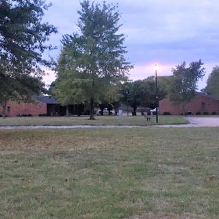 A serene view of a building surrounded by trees and open grass, under a cloudy sky.