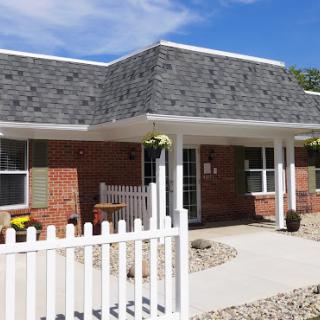 A charming residential building with a landscaped front yard, featuring a white picket fence.