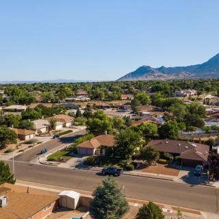 Aerial view of a suburban neighborhood with houses, trees, and mountains in the background under a clear sky.