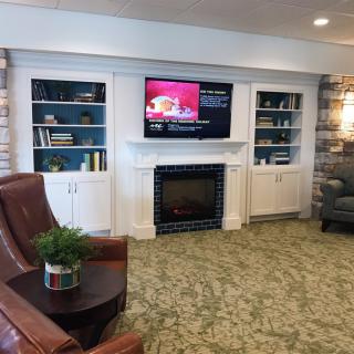 A cozy living room setting featuring a fireplace, built-in shelves with books, a flat-screen TV, and comfortable seating.