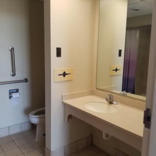 An accessible bathroom with a sink, mirror, toilet, and grab bar.