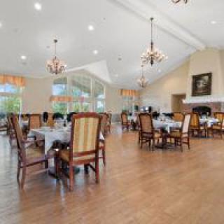 An elegant dining room with multiple tables and upholstered chairs, featuring chandeliers and a hardwood floor.