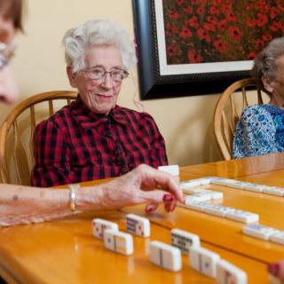 Elderly women playing dominoes at a table indoors.