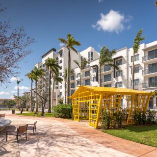 A modern residential building with palm trees and outdoor seating on a sunny day.