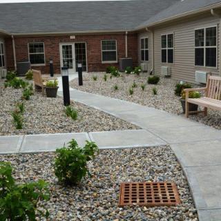 A landscaped courtyard with a pathway, benches, and shrubbery surrounded by rocks.