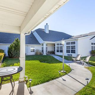 A serene outdoor patio and backyard area of a house with neatly maintained grass and seating.