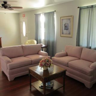 A cozy living room with two pink sofas and a wooden coffee table, complemented by light blue curtains.