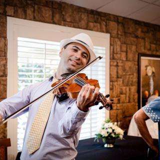 A musician wearing a hat plays the violin indoors.