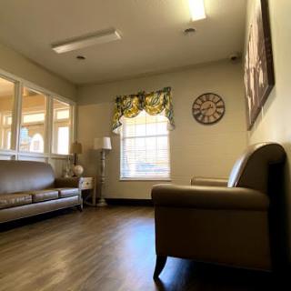 A waiting room with sofas, a window, a clock on the wall, and a lamp.