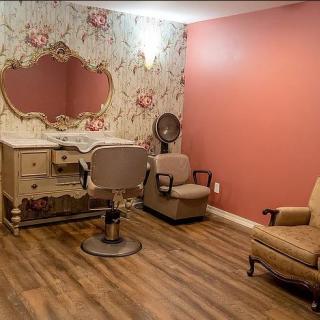A vintage-themed salon with floral wallpaper, a large mirror, and retro furniture.