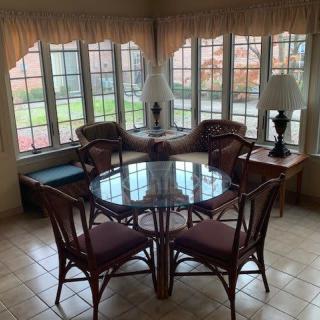 A cozy dining area with a round glass table, surrounded by chairs and flanked by large windows letting in natural light.