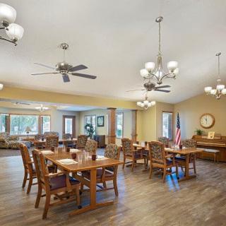 A spacious dining area with wooden tables and chairs, chandeliers, ceiling fans, and large windows.