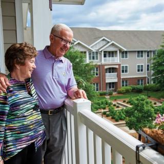 An elderly couple enjoys the view from their balcony in a retirement community.