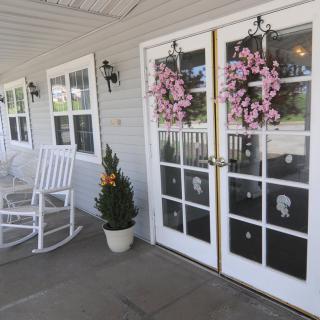 A charming porch with white rocking chairs, decorative wreaths on the doors, and potted plants.