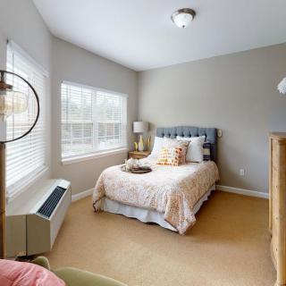 A cozy bedroom with a neatly made bed, large windows, and stylish decor.
