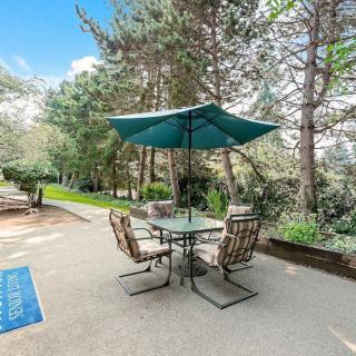 A tranquil patio area with a table and chairs under an umbrella, surrounded by lush greenery.