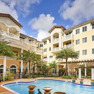 A tropical resort featuring a pool surrounded by palm trees and elegant architecture.