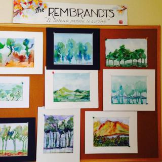 A collection of watercolor landscape paintings displayed on a bulletin board.