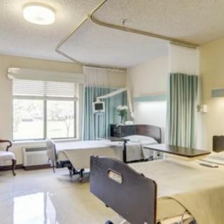 A clean and spacious hospital room with two patient beds and a large window.
