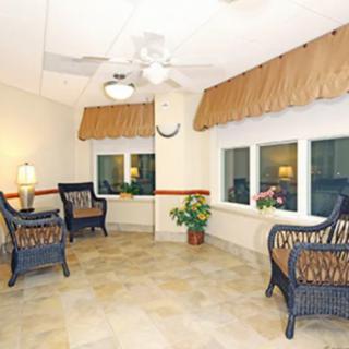 A cozy lounge area with wicker chairs, large windows, and a ceiling fan.