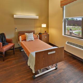 A serene and well-designed hospital patient room featuring a bed, a comfortable chair, and ample natural light.