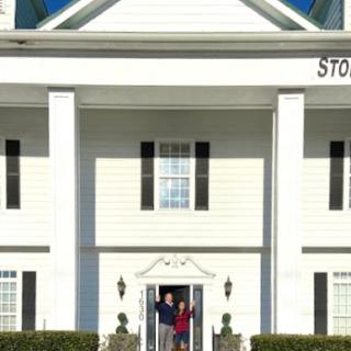 A charming white house with classic architectural features, featuring two people happily standing on the front porch.