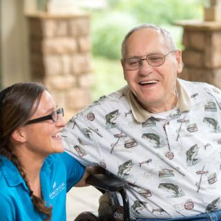 An elderly man in a wheelchair sharing a joyful moment with his caregiver outdoors.