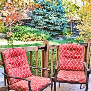 Two patio chairs on a deck overlooking a garden with autumn foliage.