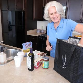 A woman unpacking groceries in the kitchen, smiling while sorting items from a shopping bag.