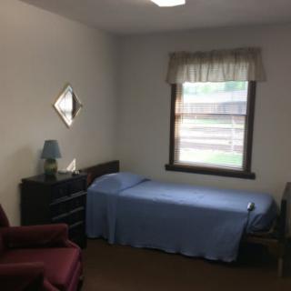 A simple bedroom with a single bed, a dresser, and a window.
