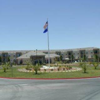 A large building with a flagpole and landscaped entrance surrounded by palm trees.
