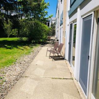 A sunny outdoor patio with chairs along a sidewalk adjacent to a building.