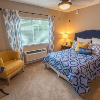 A cozy bedroom with a blue and white patterned bedspread, a yellow chair, and soft lighting.
