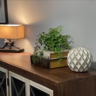 A cozy home interior with a warm-lit lamp, decorative plant, and books on a wooden cabinet.