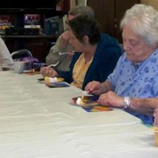 A group of elderly individuals enjoying a meal together at a long table.