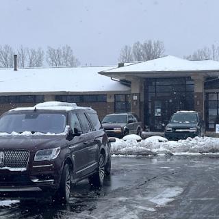 A snowy scene featuring parked cars in front of a building.