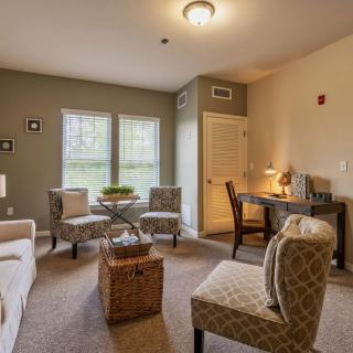 A cozy living room with comfortable seating, a workspace, and ample natural lighting.